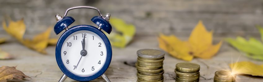 Alarm clock and money coins on wooden rustic old table with autumn leaves. Time is money autumn style comcept. Discount time concept. Time for fall autumn savings. Time to make money.